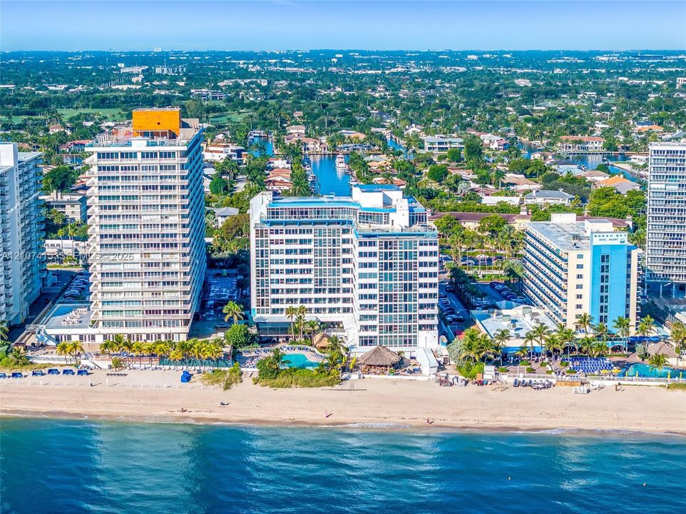 Aerial perspective of beachfront high-rise featuring immediate ocean access, a ground-level swimming pool, and tropical landscaping