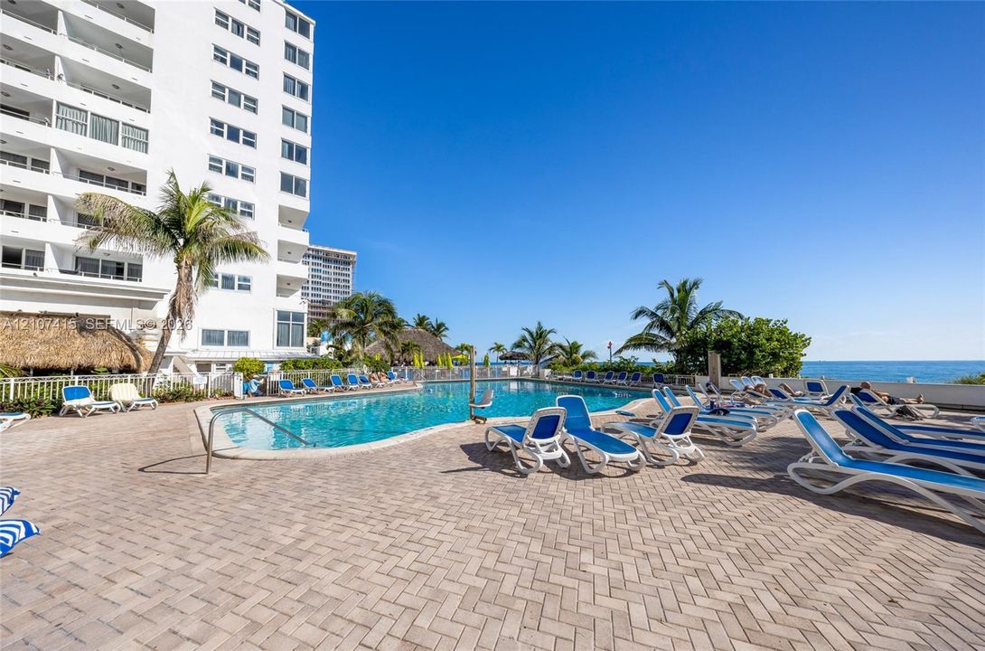 Swimming pool with herringbone-patterned paver decking, surrounding mature palm trees, and coastal proximity