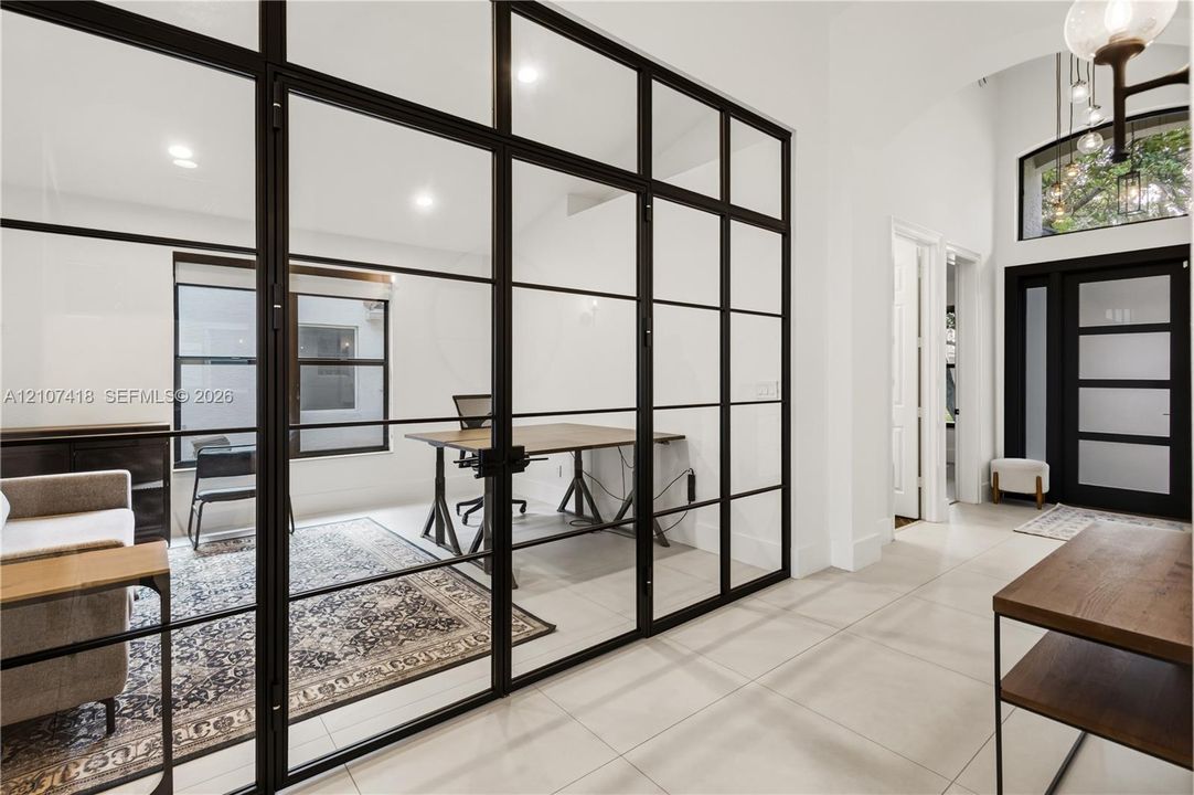 Floor-to-ceiling iron-frame glass room divider, recessed lighting, tile flooring, arched entryway, and front door with glass inserts