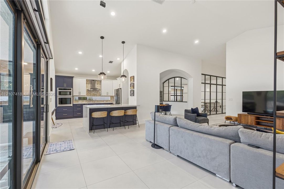 Open-concept kitchen featuring two-toned cabinetry, a large central island, recessed lighting, glass-paneled interior partitions, and porcelain tile flooring