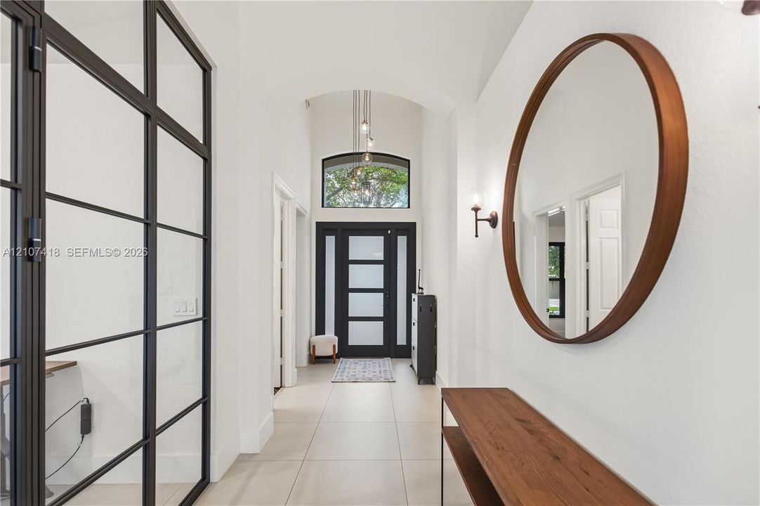 Entryway featuring large-format tile flooring, a vaulted ceiling with a pendant light, an arched transom window, and a metal-framed glass partition wall
