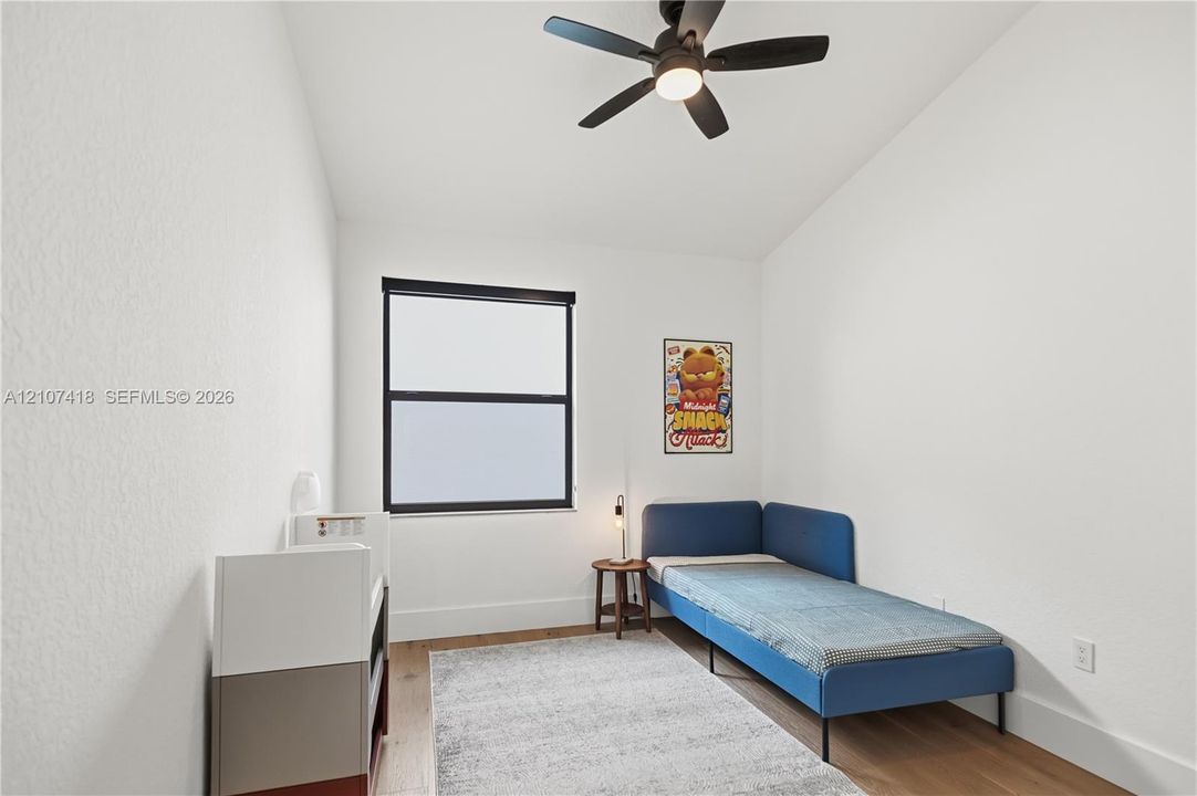 Room featuring wood-finish flooring, a matte black multi-blade ceiling fan with integrated lighting, and a window with a matte black frame