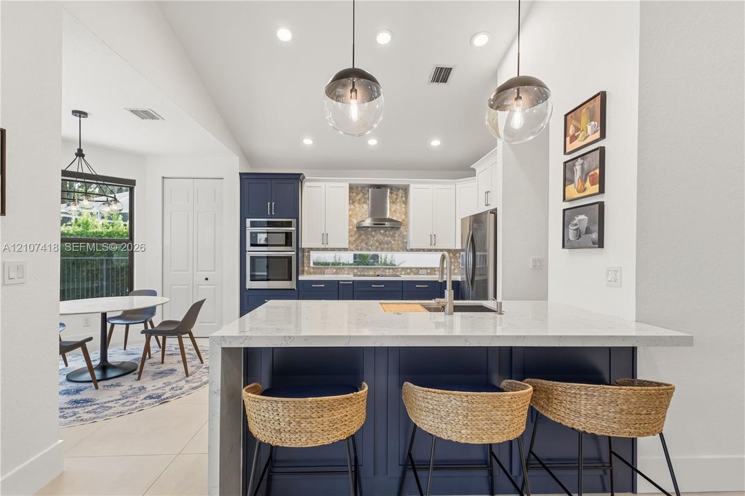Kitchen featuring a central island with a solid surface countertop, contrasting navy and white cabinetry, a built-in double wall oven, patterned tile backsplash, and oversized globe pendant lighting