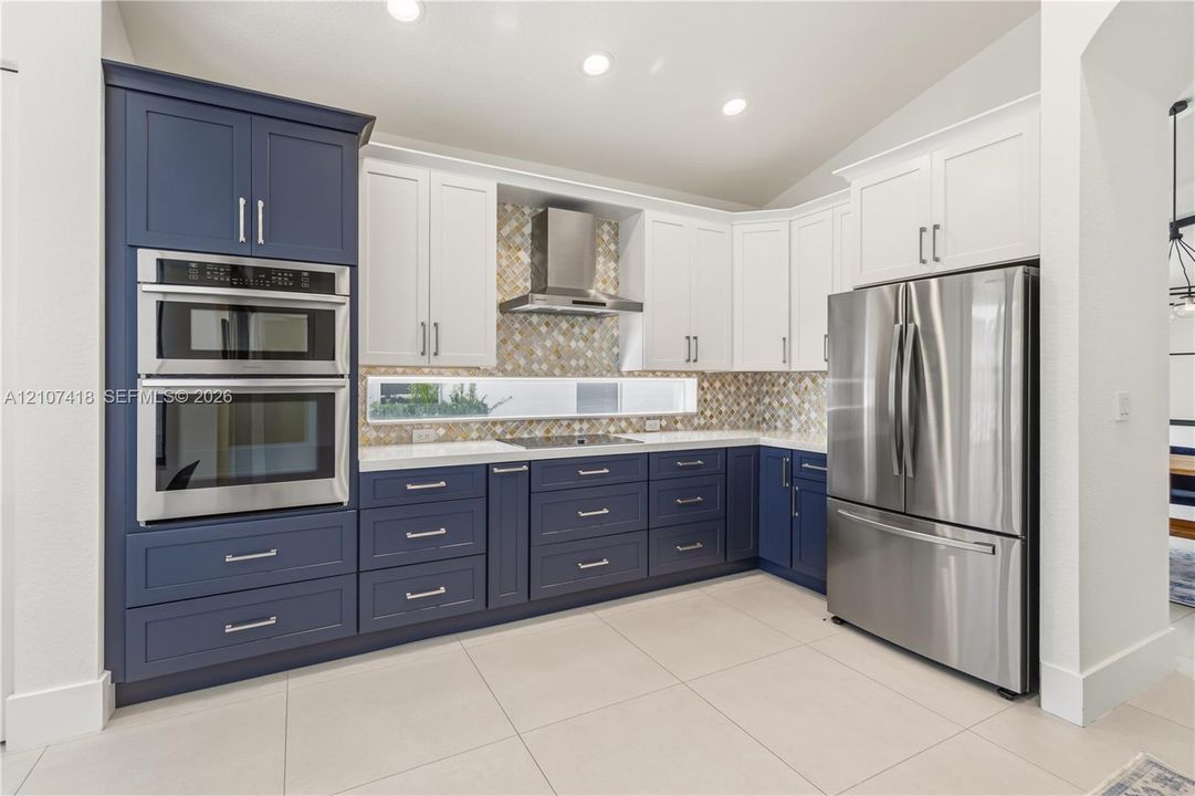 Kitchen featuring two-tone cabinetry, stainless steel double wall oven, stainless steel refrigerator, patterned mosaic tile backsplash, and quartz countertops
