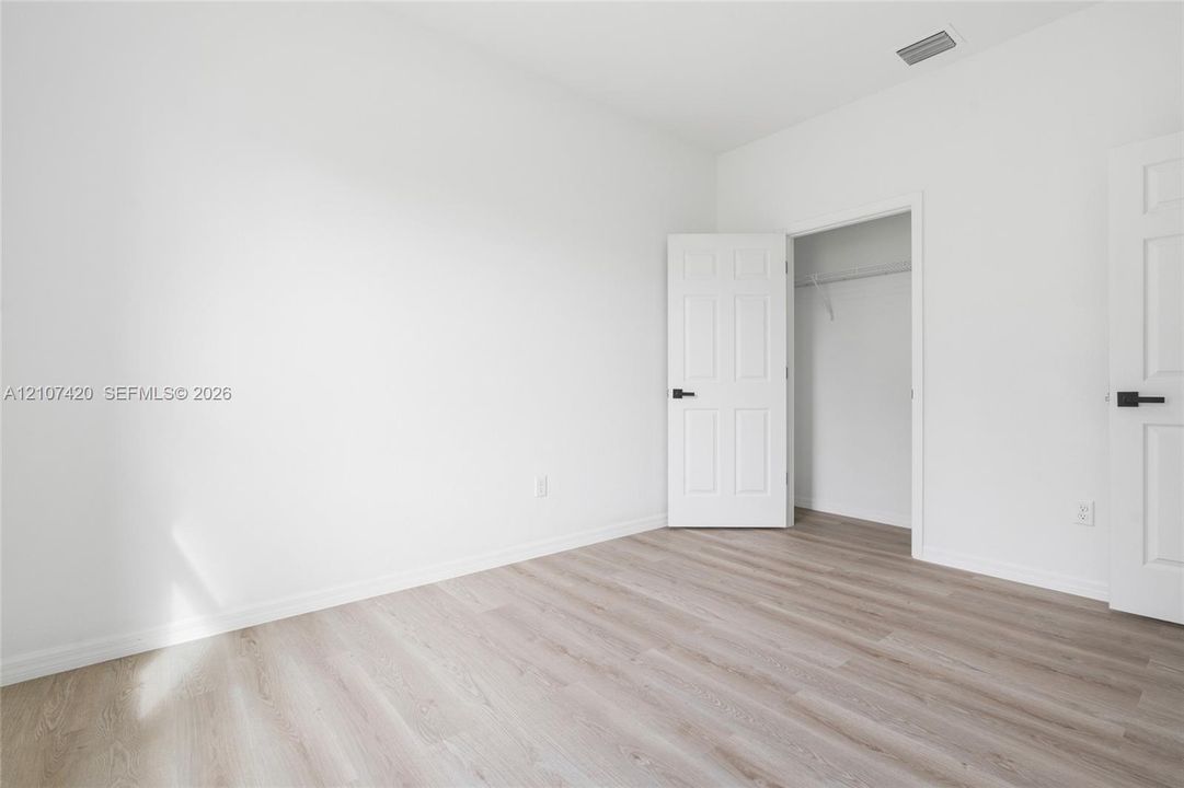 Neutral-toned wood-finish flooring, white walls, and interior doors featuring matte black hardware, including a closet with wire shelving