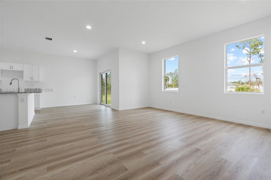 Open-concept interior featuring wood-finish flooring, recessed lighting, expansive windows, glass sliding door, and kitchen peninsula with stone-surface countertop