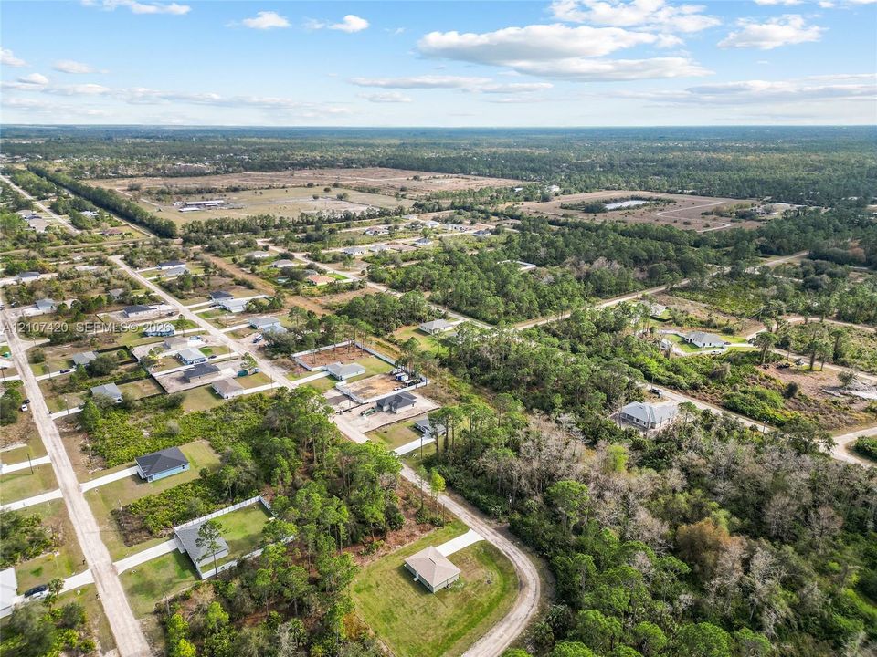 Aerial perspective of a residential lot featuring expansive cleared acreage, mature native vegetation, and unpaved roadway access