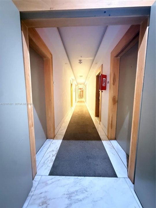 Hallway featuring natural wood-finish door frames, stone-patterned tile flooring, and recessed ceiling lighting