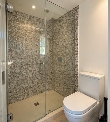 Walk-in shower featuring a frameless glass door, full-height mosaic tile surround, rainfall shower head, and recessed lighting