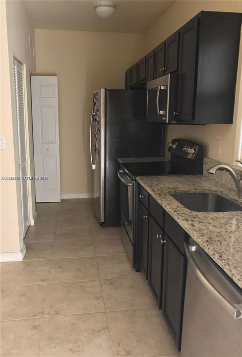 Kitchen featuring dark-finish cabinetry, stone-surface countertops, stainless steel appliances, a recessed stainless steel sink, and tile flooring