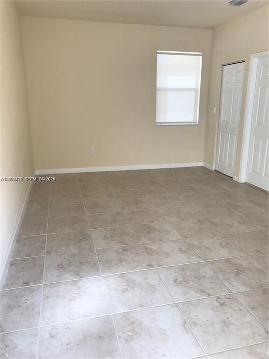 Interior space featuring neutral wall tones, large-format ceramic tile flooring, a single window with roller shade, and two interior doors with paneled detailing