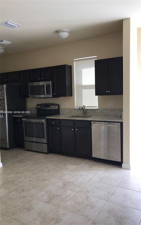 Kitchen featuring dark-finish cabinetry, stone-surface countertops, stainless steel appliances, and tile flooring