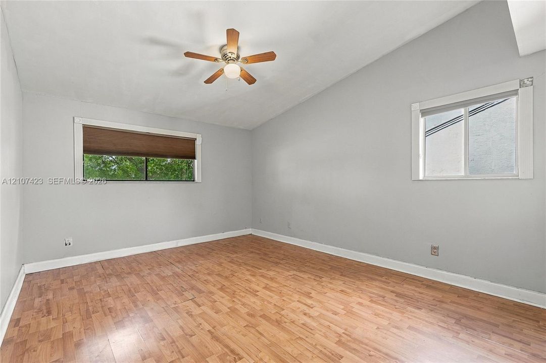 Vaulted ceiling featuring a central wood-finish ceiling fan with integrated lighting, wood-finish flooring, and dual windows
