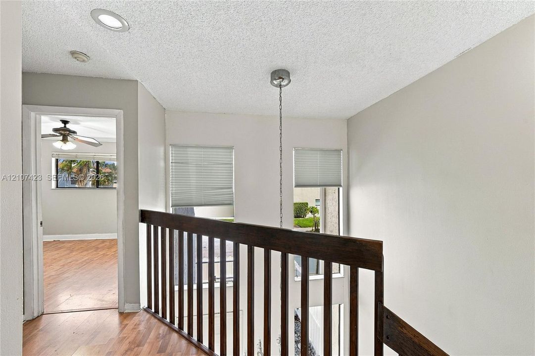 Landing area featuring wood-finish flooring, recessed lighting, a stained wood railing, and dual vertical windows