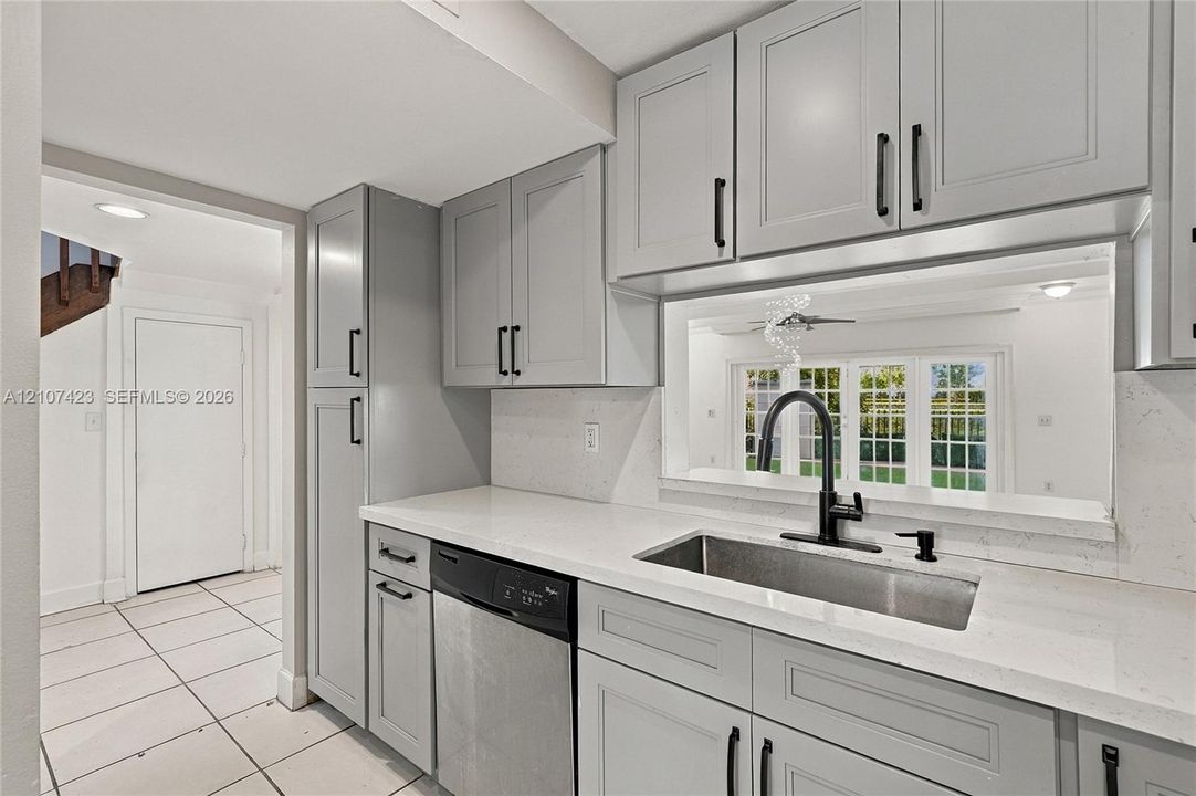 Kitchen featuring grey Shaker-style cabinetry, quartz countertops, stainless steel undermount sink with matte black faucet, and built-in dishwasher