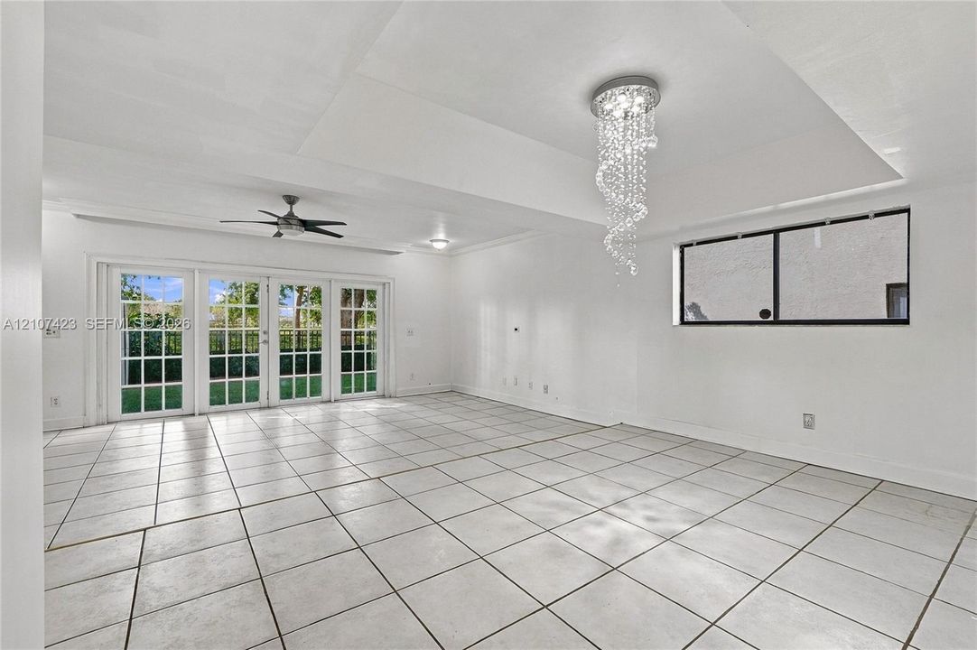 Interior space featuring tile flooring, a tray ceiling, crystal chandelier, ceiling fan, and multipane French doors