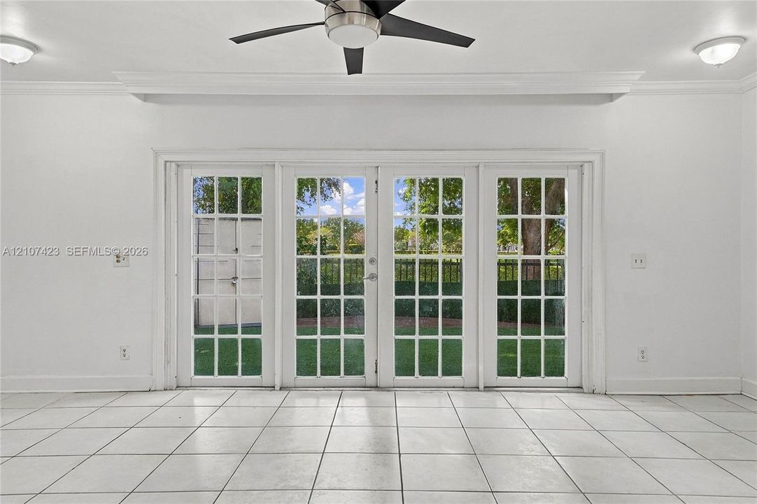 Set of four glass-paned French doors, neutral tile flooring, recessed and flush-mount ceiling lighting, and a multi-blade ceiling fan with integrated light