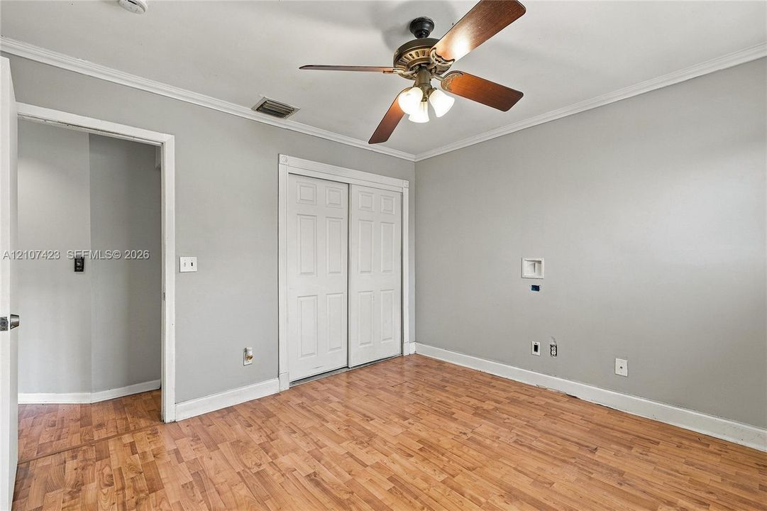 Interior space featuring wood-finish flooring, crown molding, a central ceiling fan with integrated lighting, and a double-panel closet door