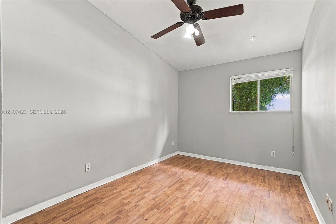 Room with wood-finish flooring, neutral wall paint, vaulted ceiling, multi-blade ceiling fan with integrated lighting, and horizontal sliding window