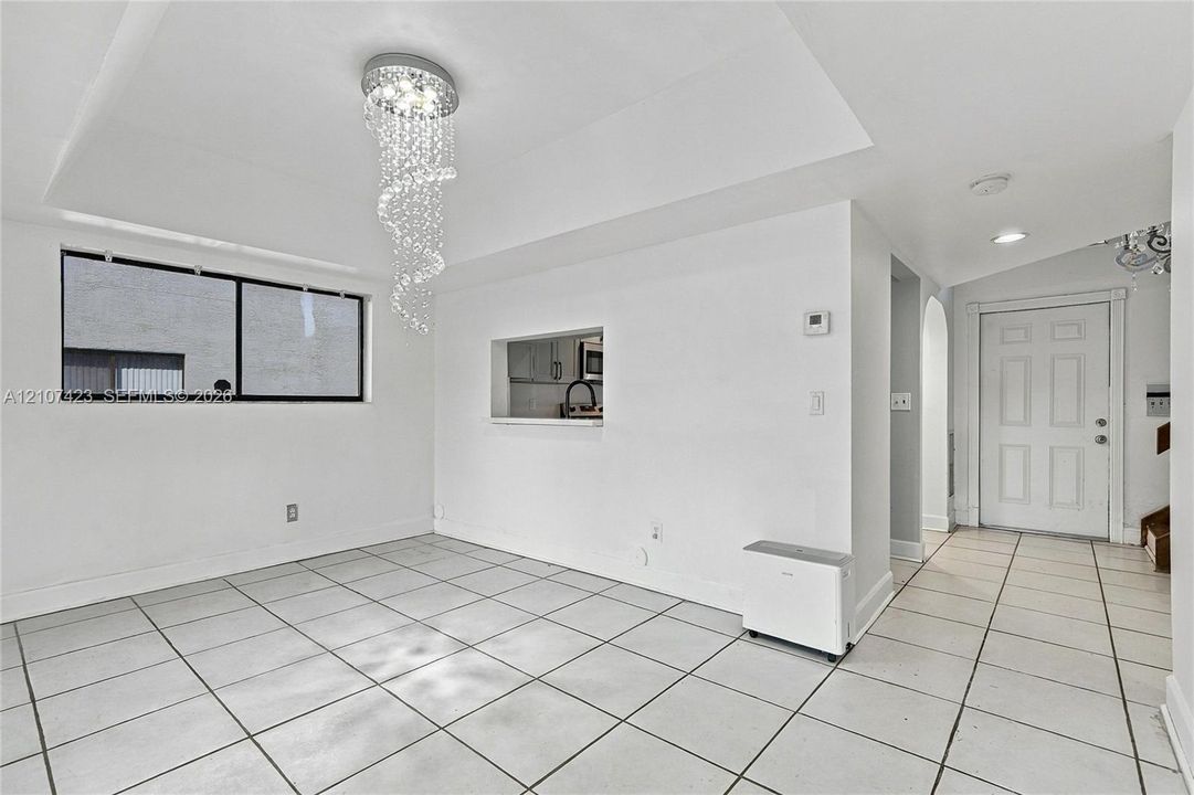 Open interior space featuring large-format ceramic tile flooring, a recessed ceiling with a crystal drop chandelier, and a cut-out wall opening