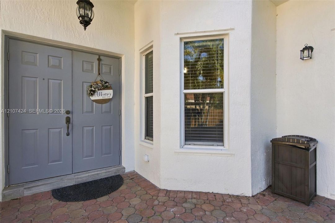 Entryway featuring a double-door entrance with paneled detailing, decorative exterior wall-mounted lighting, and a multi-toned paver porch