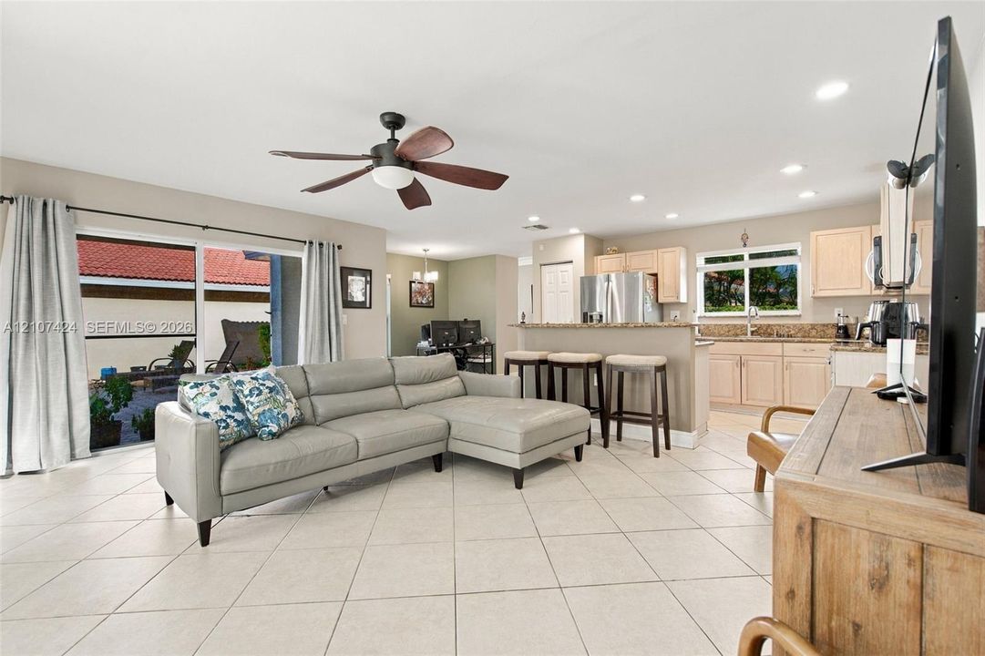 Open-concept interior featuring light-toned tile flooring, recessed ceiling lighting, a multi-blade ceiling fan, and sliding glass doors