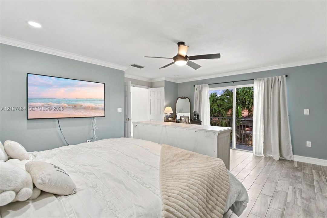 Living space featuring wood-finish tile flooring, crown molding, a central ceiling fan with integrated lighting, and a sliding glass door providing external access