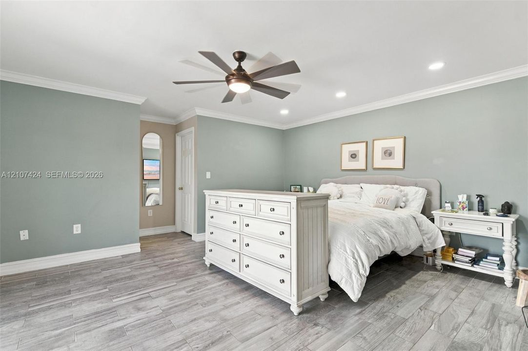 Oversized bedroom featuring recessed lighting, crown molding, wood-finish tile flooring, and a multi-blade ceiling fan