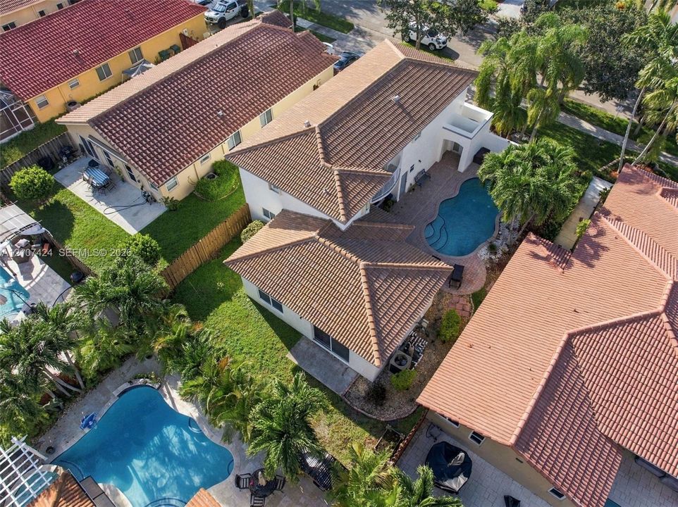 Aerial perspective of a two-story residence featuring a tile roof, an in-ground swimming pool, and stone paver decking