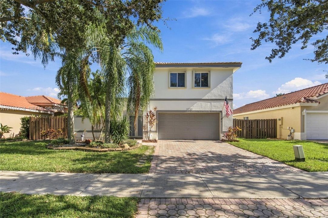Two-story stucco exterior featuring a multi-car garage, concrete paver driveway, tiled roof, and mature palm landscaping