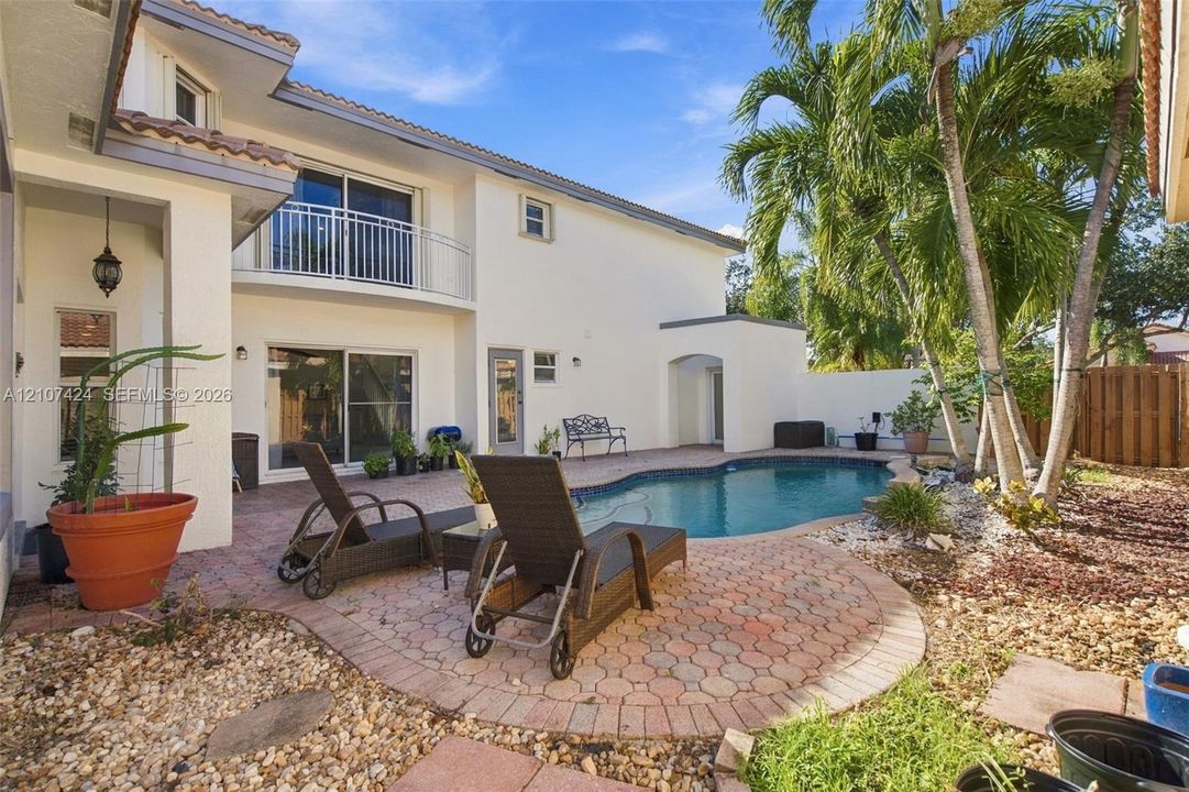 Rear exterior featuring a stucco facade, second-story balcony with metal railings, in-ground pool, and a paved stone patio