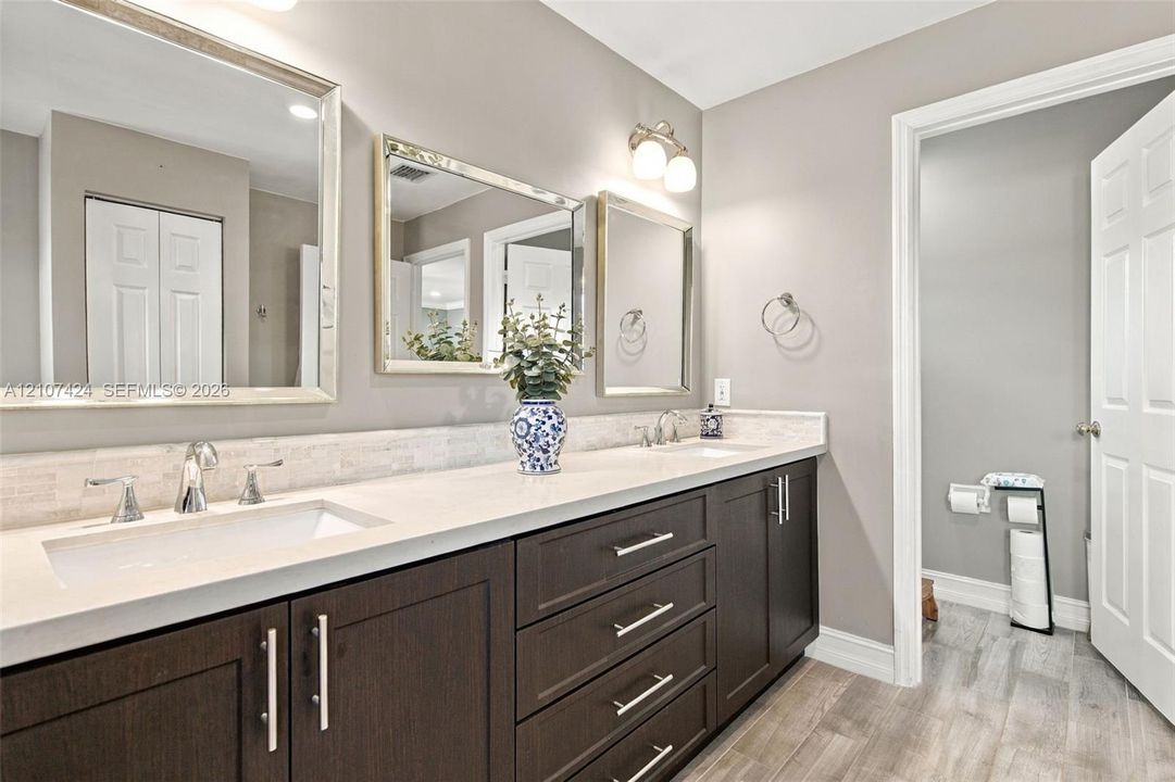 Double vanity featuring dark espresso cabinetry, stone-finish countertops, dual rectangular undermount sinks, polished chrome hardware, and three separate rectangular mirrors
