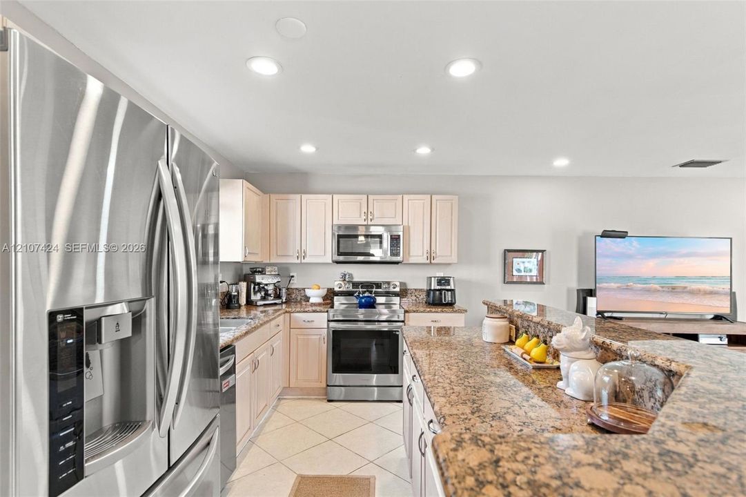 Kitchen featuring stone-finish countertops, stainless steel refrigerator, built-in microwave, range, and recessed lighting