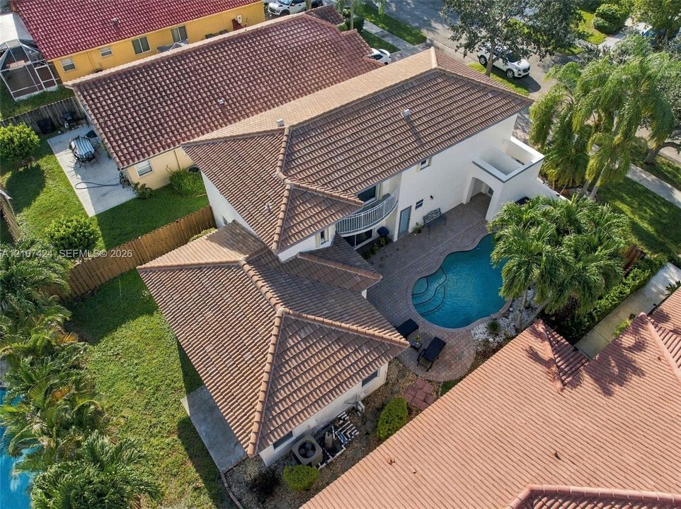 Two-story residence featuring a tile roof, an upper-level balcony, a swimming pool with integrated spa, and paver hardscaping