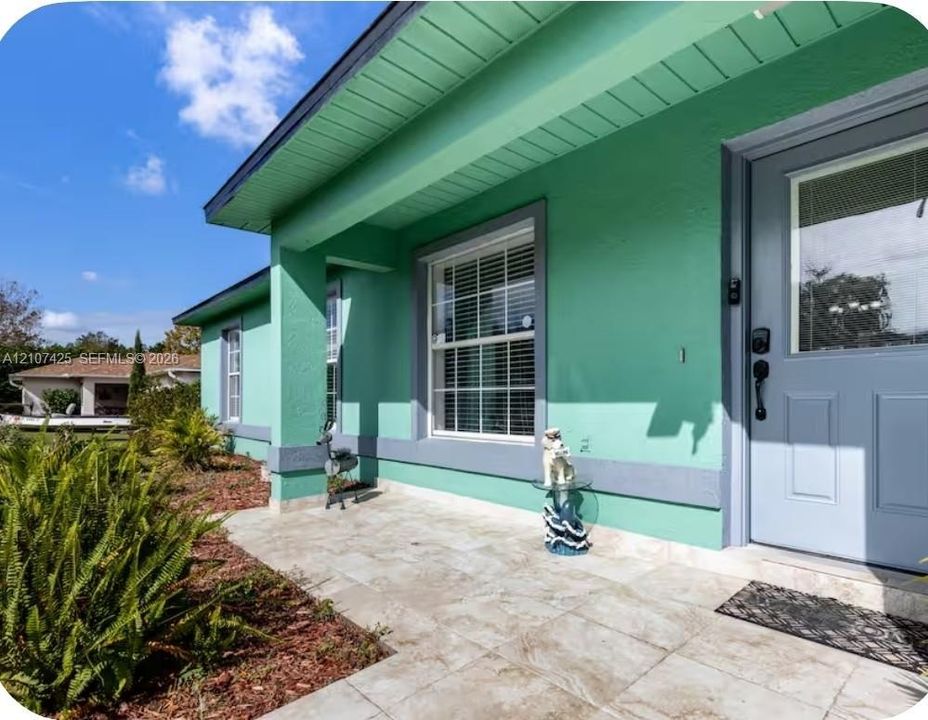 Covered front entryway featuring large-format tile flooring, a solid-core front door with an integrated glass pane, and multi-pane windows with contrasting trim