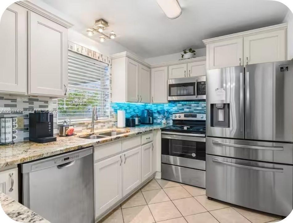 Kitchen featuring off-white cabinetry, stone-finish countertops, stainless steel appliances, multi-toned horizontal tile backsplash, and ceramic tile flooring