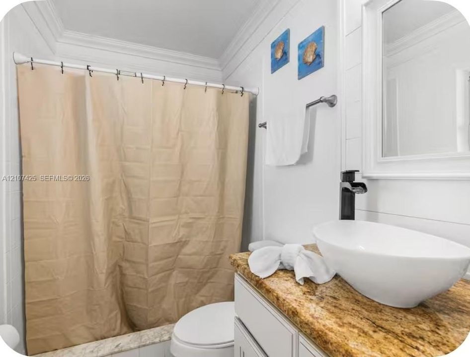 Bathroom featuring an oval vessel sink, matte black faucet, stone-finish countertop, white cabinetry, and shiplap-style wall paneling