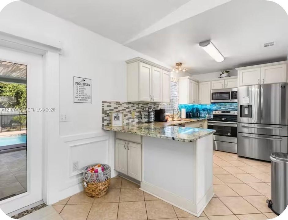 Kitchen featuring white cabinetry, stone-surface countertops, mosaic tile backsplash, stainless steel appliances, and tile flooring