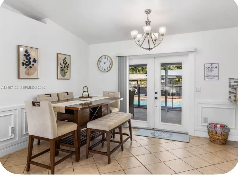 Dining area featuring neutral tile flooring, wainscoting, a multi-arm chandelier, and glass-paneled double doors