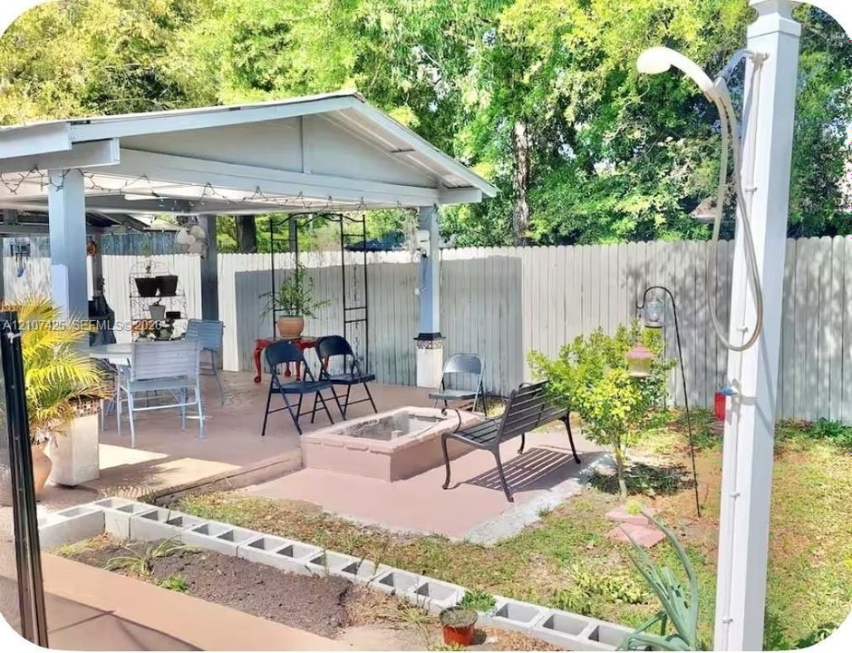 Covered patio featuring a solid roof structure, outdoor fire pit, exterior shower, and concrete hardscaping enclosed by a perimeter fence