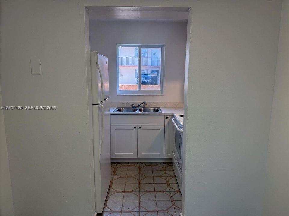 Kitchen featuring white shaker-style cabinetry, a dual-basin stainless steel sink, stone-finish countertops, and ceramic tile flooring