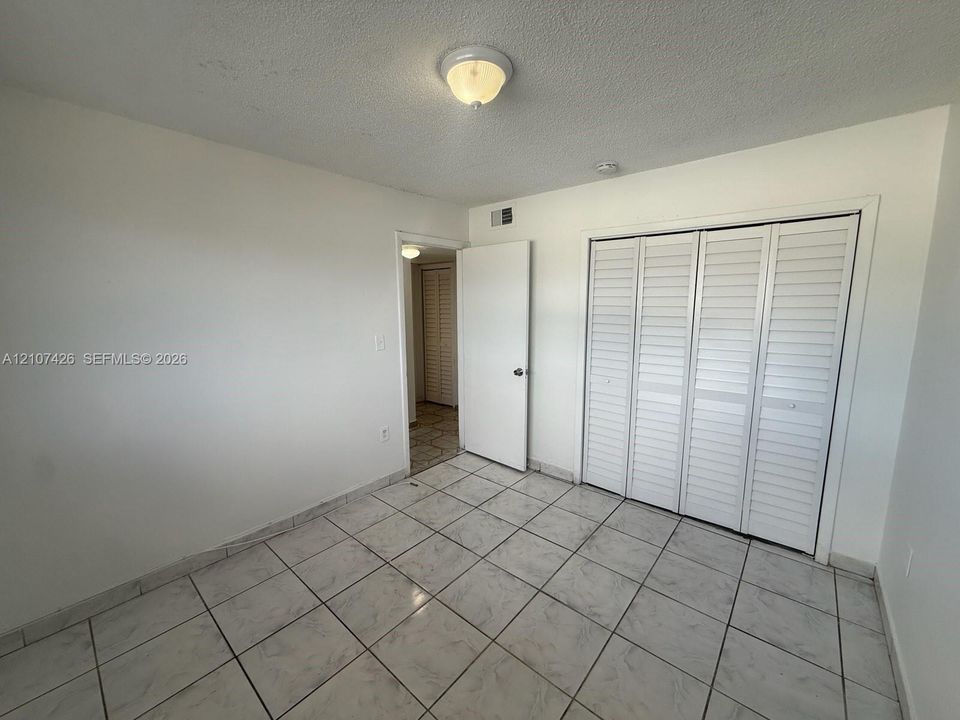 Tile flooring, white louvered-style closet doors, and flush-mount lighting fixture