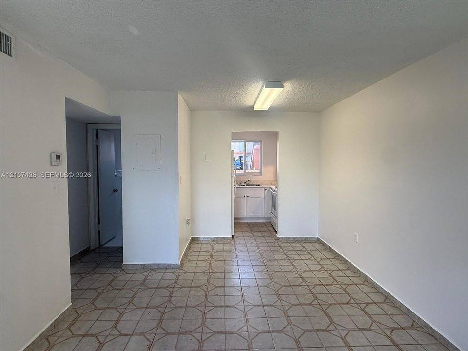 Interior area featuring neutral wall paint, geometric-patterned tile flooring, flush-mount overhead lighting, and white cabinetry in the kitchen area