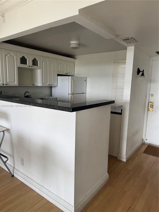 Kitchen featuring a peninsula with dark stone-finish countertop, white cabinetry with glass-front detailing, wood-finish flooring, and a wall-mounted light fixture