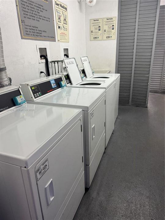 Communal laundry room featuring multiple commercial-grade top-load washers and dryers, louvered closet doors, and smooth-finish flooring