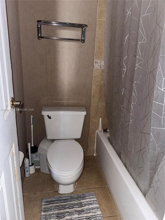 Full bathroom featuring a white porcelain toilet, a standard-size soaking tub with a white surround, neutral-toned wall tiles, and a polished metal towel rack