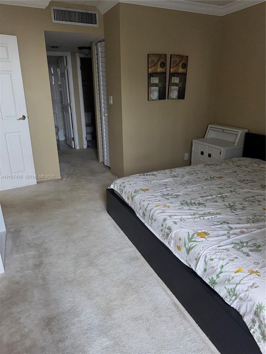 Room featuring neutral-toned walls, carpeting, crown molding, and louvered closet doors