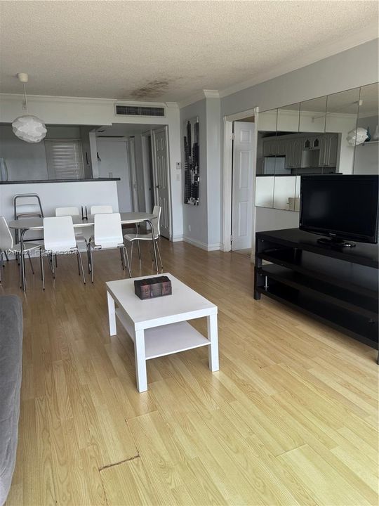 Open-concept interior featuring light wood-finish flooring, a mirrored wall accent, and a built-in kitchen pass-through counter