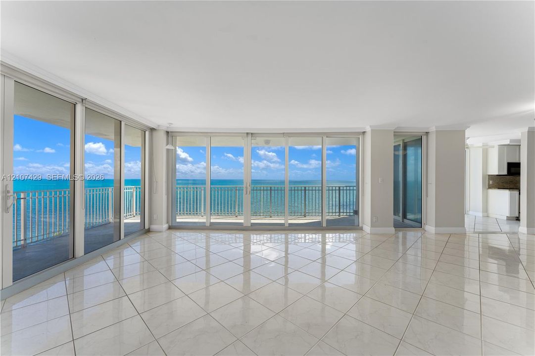 Expansive interior space featuring large-format tile flooring, crown molding, and floor-to-ceiling glass panel walls with access to a balcony