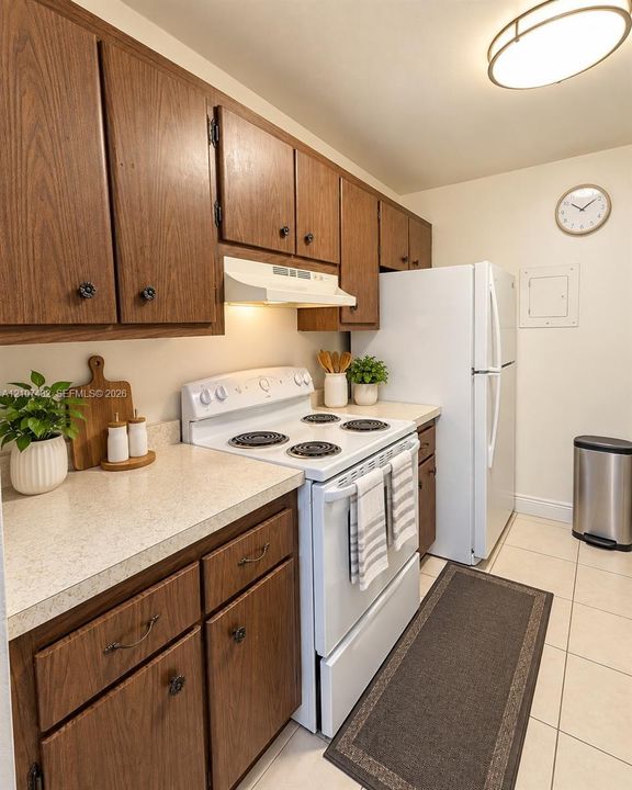 Kitchen featuring wood cabinetry, stone-finish countertops, tile flooring, and integrated white appliances including a range and refrigerator